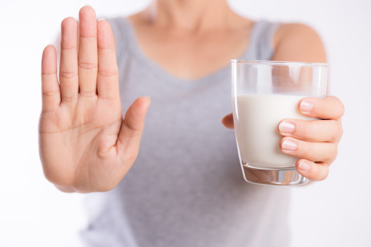Woman hand holding glass of milk having bad stomach ache because of Lactose intolerance and another hand shows stop sign health problem with dairy food products Healthcare and medical concept