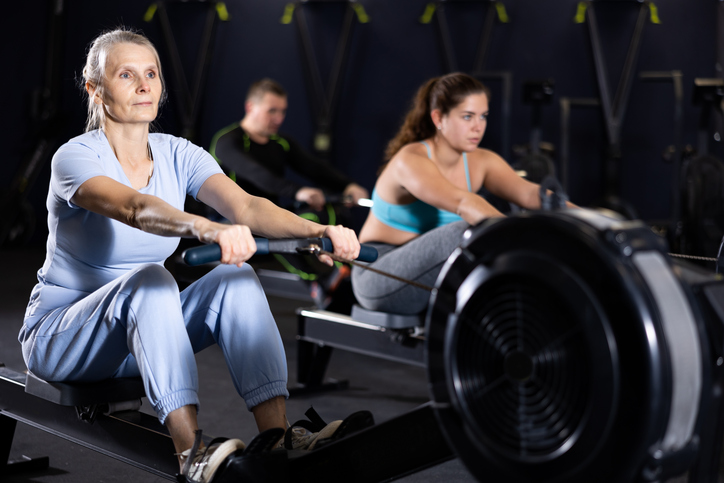 Concentrated sporty senior woman working out on rowing machine during total body workout in gym Active lifestyle of older adults concept