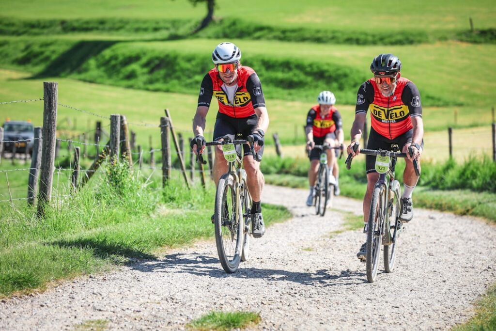 Cyclists riding on a gravel road through green hills.